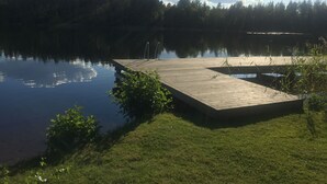 Une jetée en bois s’étendant dans un lac paisible, entourée d’une végétation luxuriante et d’une zone boisée.