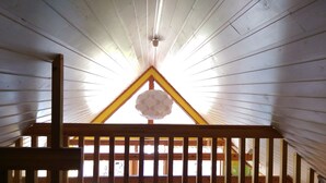 Une pièce dotée d’un plafond en pente, de poutres en bois et d’une fenêtre triangulaire ornée d’un globe décoratif.