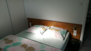 Sängyssä on puinen pääty, kaksi kukallista koristetyynyä ja ananaskuviollinen päiväpeite.