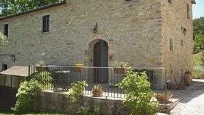 Un bâtiment en pierre doté d’une porte centrale et de fenêtres, entouré d’un petit jardin agrémenté de plantes en pot.