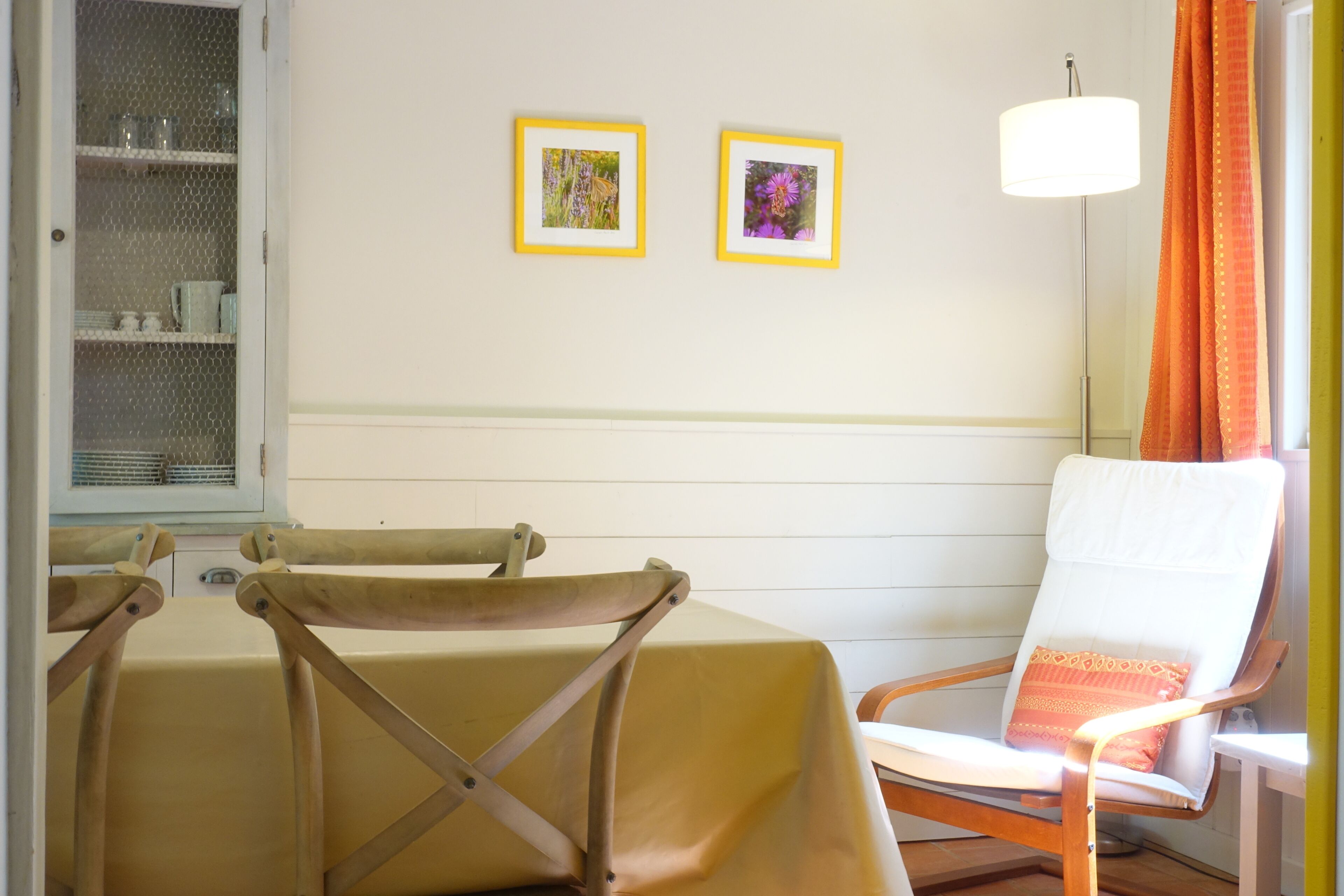 Ein Zimmer mit einem Tisch, zwei Stühlen, einer Lampe und zwei gerahmten Bildern an der Wand.