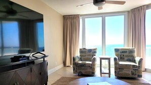 Ein Hotelzimmer mit einem großen Flachbildfernseher, zwei sesseln im Strandhausstil, einem kleinen Beistelltisch und einem runden Couchtisch.