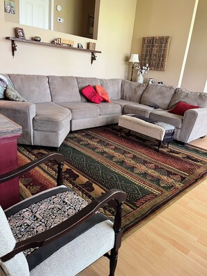 A living room with a grey sectional sofa, a patterned rug, and a wooden chair.