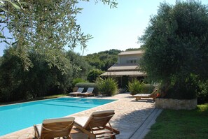 Una piscina con lettini, circondata dal verde e con una casa sullo sfondo.