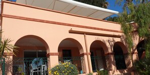Un edificio con fachada color melocotón, tres ventanas arqueadas y un patio cubierto.