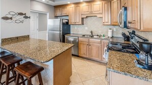 Una cocina con encimeras de granito, armarios de madera, refrigerador de acero inoxidable, lavavajillas y estufa.