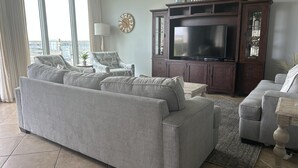 Una sala de estar con un amplio sofá seccional gris, un televisor sobre un mueble de madera y un ventilador de techo.