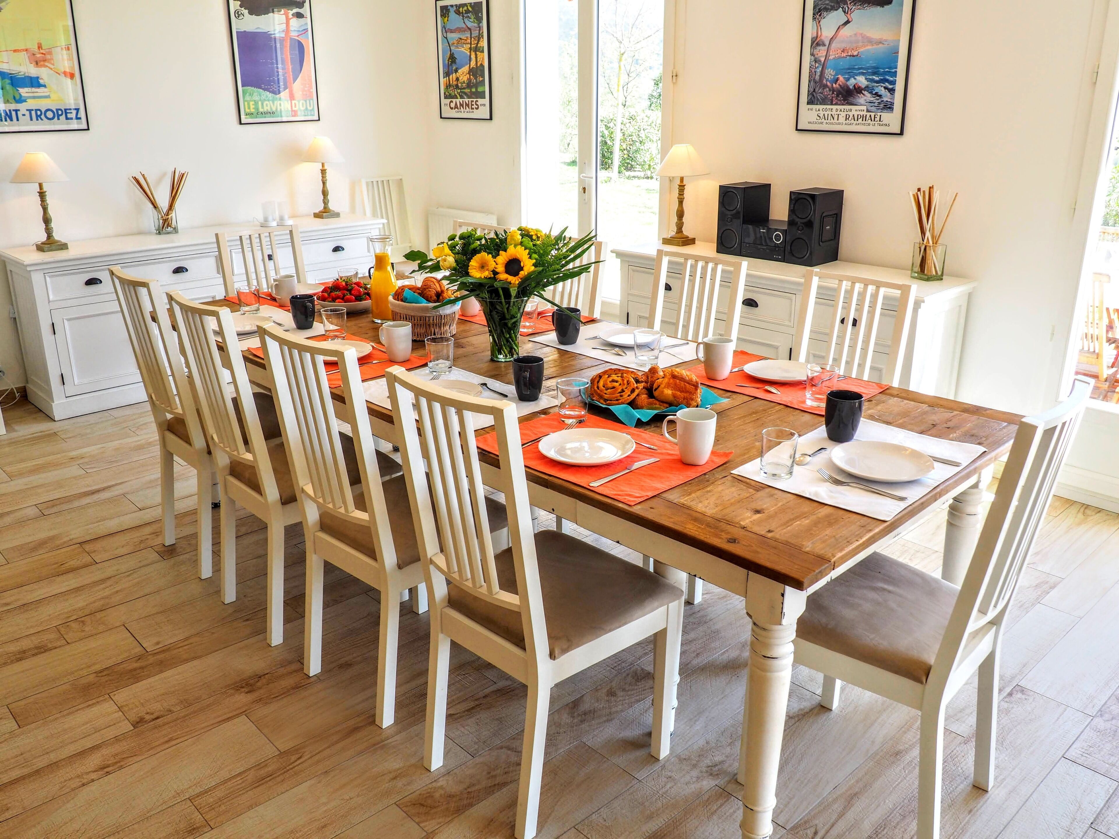 A dining area with a wooden table set for six, surrounded by white chairs.