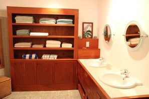 Une coiffeuse en bois avec deux vasques, un miroir et des étagères où sont pliées des serviettes.