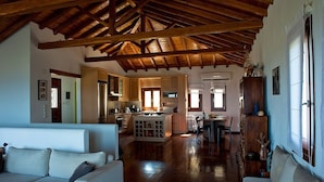 A spacious living area with a wooden ceiling, a kitchen in the background, and a dining area with a table and chairs.