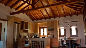 A spacious kitchen with wooden beams, a central island, and a dining area with a table and chairs.