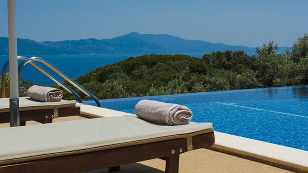 A poolside area with lounge chairs and towels, overlooking a mountainous landscape.