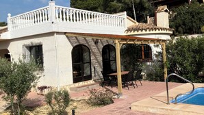 Un edificio blanco con un patio cubierto, piscina y jardín.