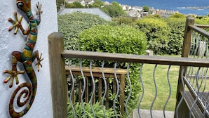 Een balkon met een decoratieve hagedis, weelderige begroeiing en uitzicht op de zee en huizen.