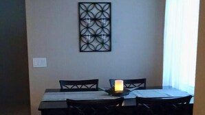 Un coin repas avec une table et quatre chaises, un élément décoratif mural au-dessus de la table et une bougie allumée sur la table.