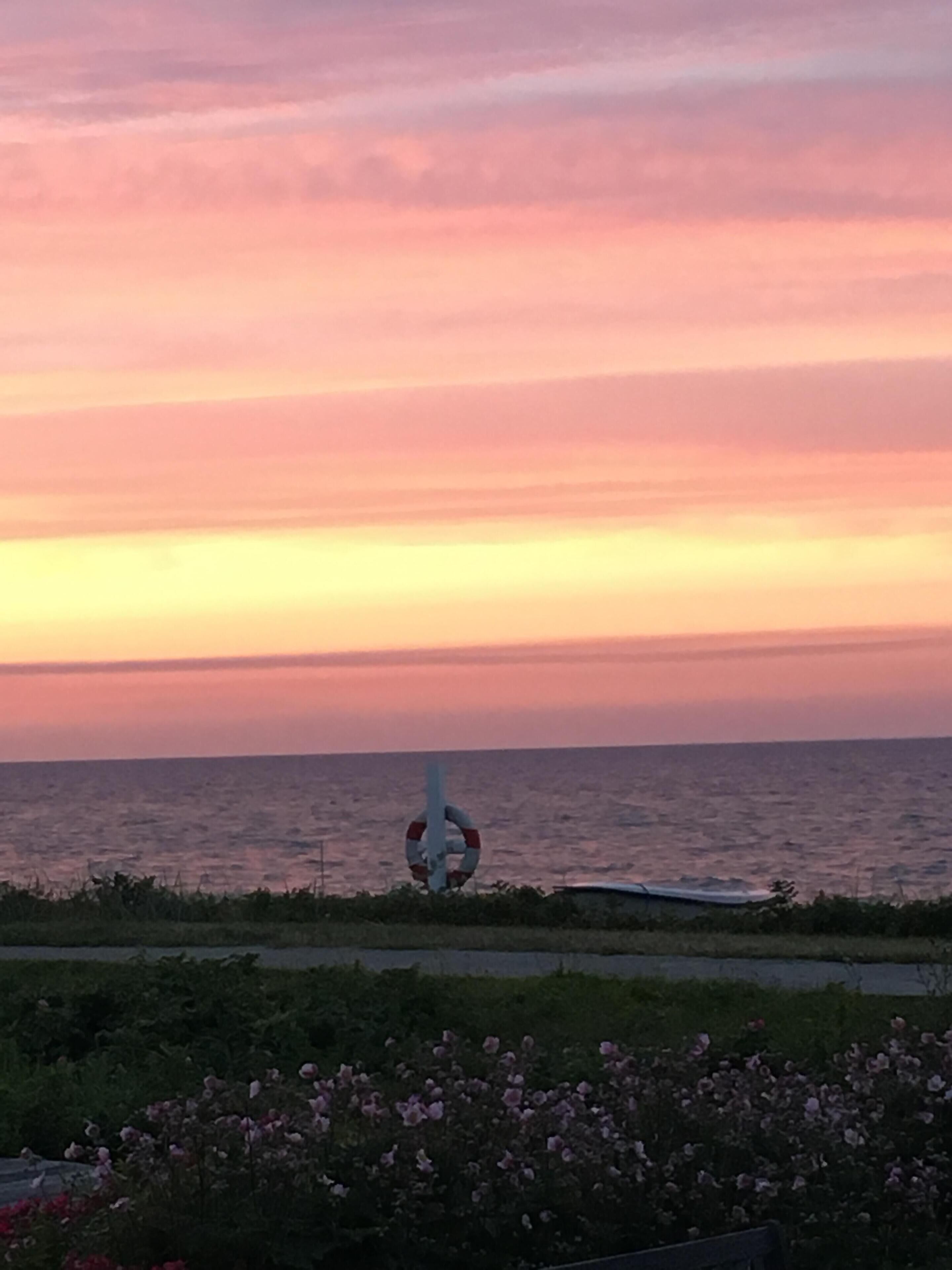 A sunset view over the ocean with a lifebuoy sculpture in the foreground.