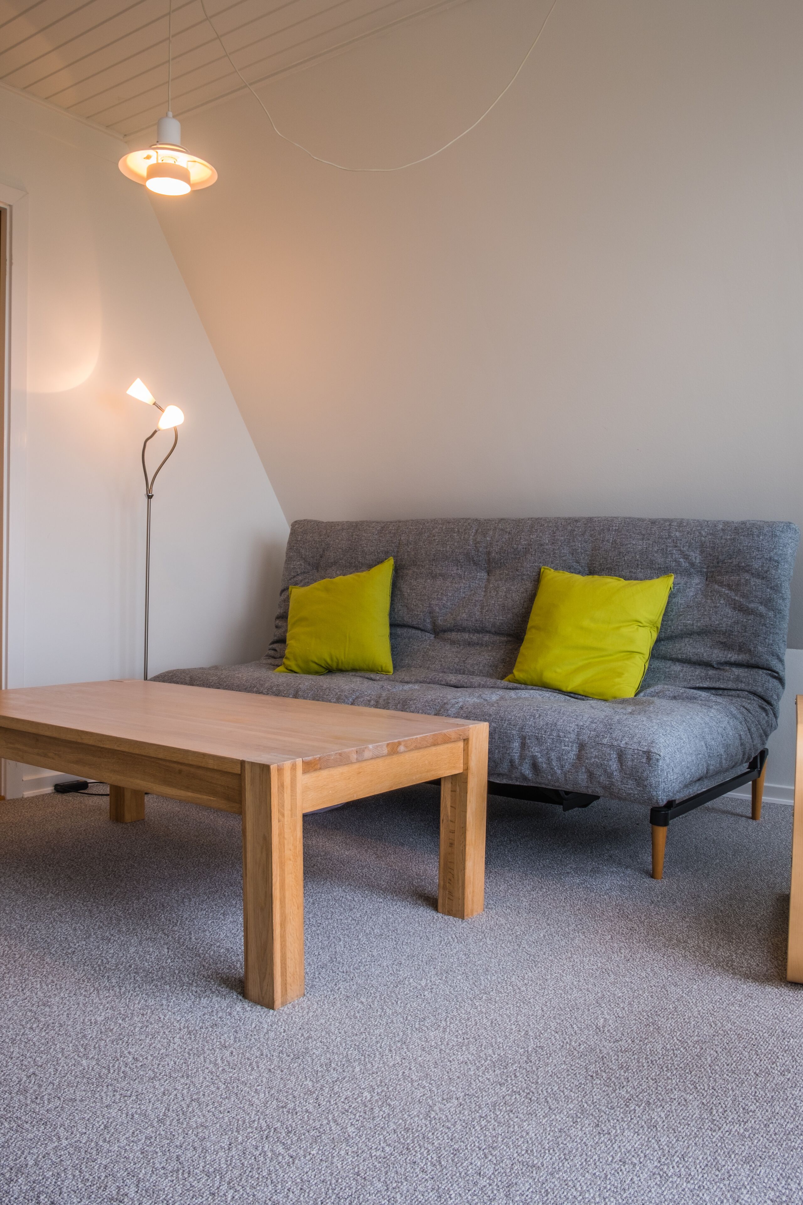 A room with a grey sofa, two bright yellow pillows, a wooden table, and a floor lamp.