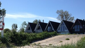 En rad med stugor som ligger vid stranden, med en sandstig som leder fram till dem, och som är omgivna av grönska.