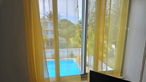 Habitación con ventana que da a una piscina, cortinas y un televisor.