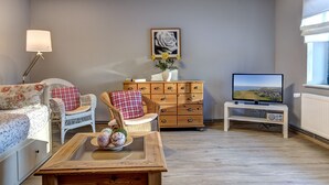 A living room with a sofa, two wicker chairs, a wooden coffee table, a TV on a stand, a dresser, and a framed picture on the wall. - Vacation under the thatched roof on the backwater opposite the island of Usedom (Lassan)