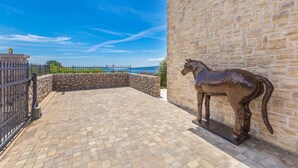 A courtyard with a stone wall, a metal fence, and a bronze horse statue. - Villa CAVALLO with pool and sea view (Linardići)