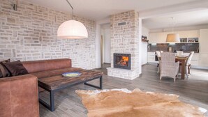 A living room with a stone wall, a fireplace, a leather sofa, a wooden coffee table, and a cowhide rug. - Villa CAVALLO with pool and sea view (Linardići)