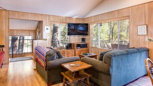 A cozy living room with wooden walls, a large TV, a sofa, a coffee table, and a bookshelf. - (64) River Lodge at The Redwoods In Yosemite (Yosemite National Park)