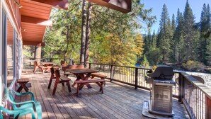 A wooden deck with picnic tables and chairs, overlooking a forested area with a river. - (64) River Lodge at The Redwoods In Yosemite (Yosemite National Park)