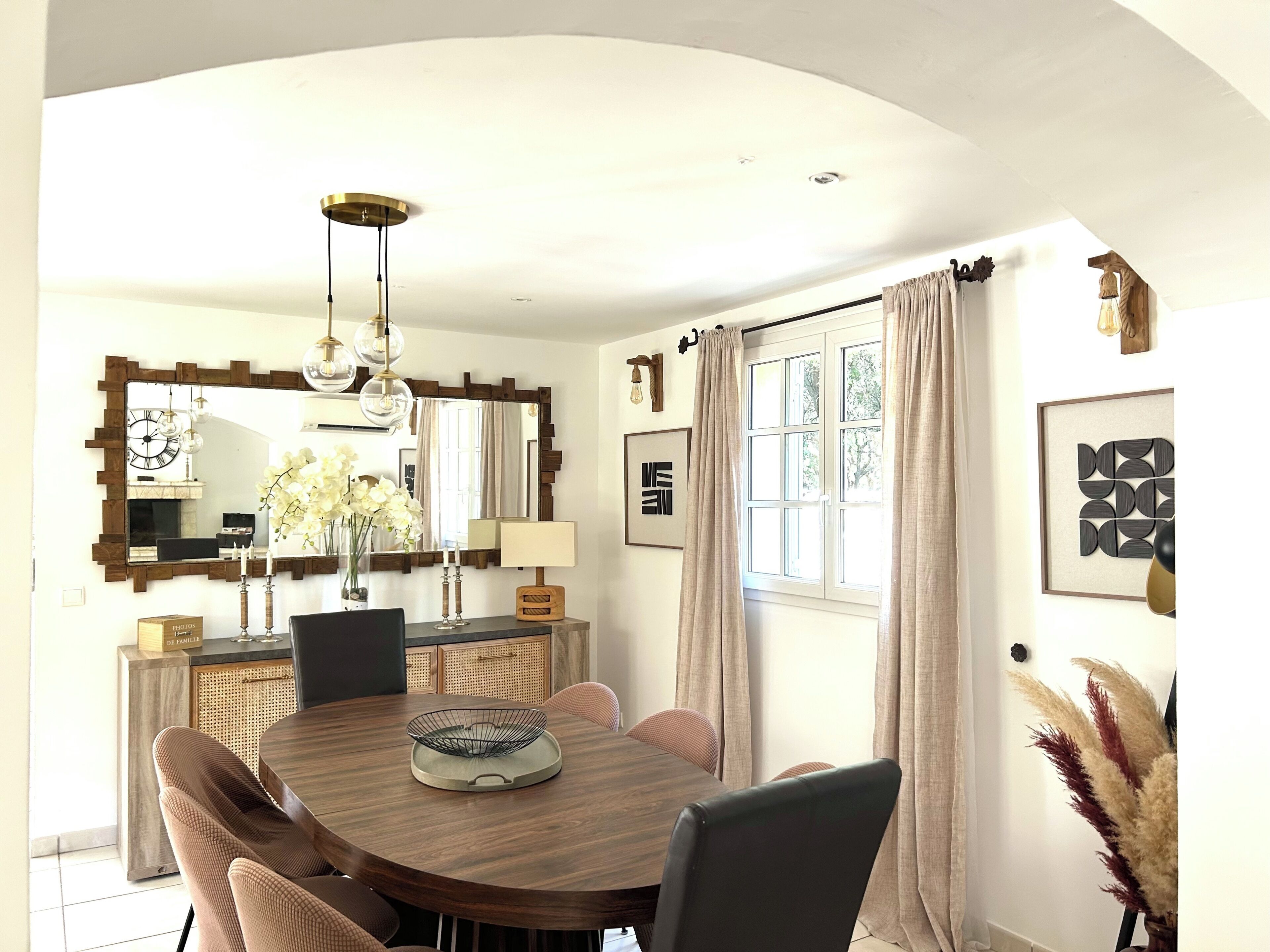 A dining area with a round table, chairs, a chandelier, and a large mirror.