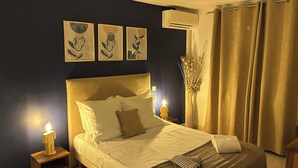 Une chambre à coucher comprenant un lit, des tables de chevet, un climatiseur fixé au mur et des œuvres d’art.