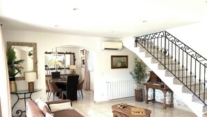 Un salon comprenant un canapé, une table basse, un coin repas avec des chaises et un escalier avec une rampe.
