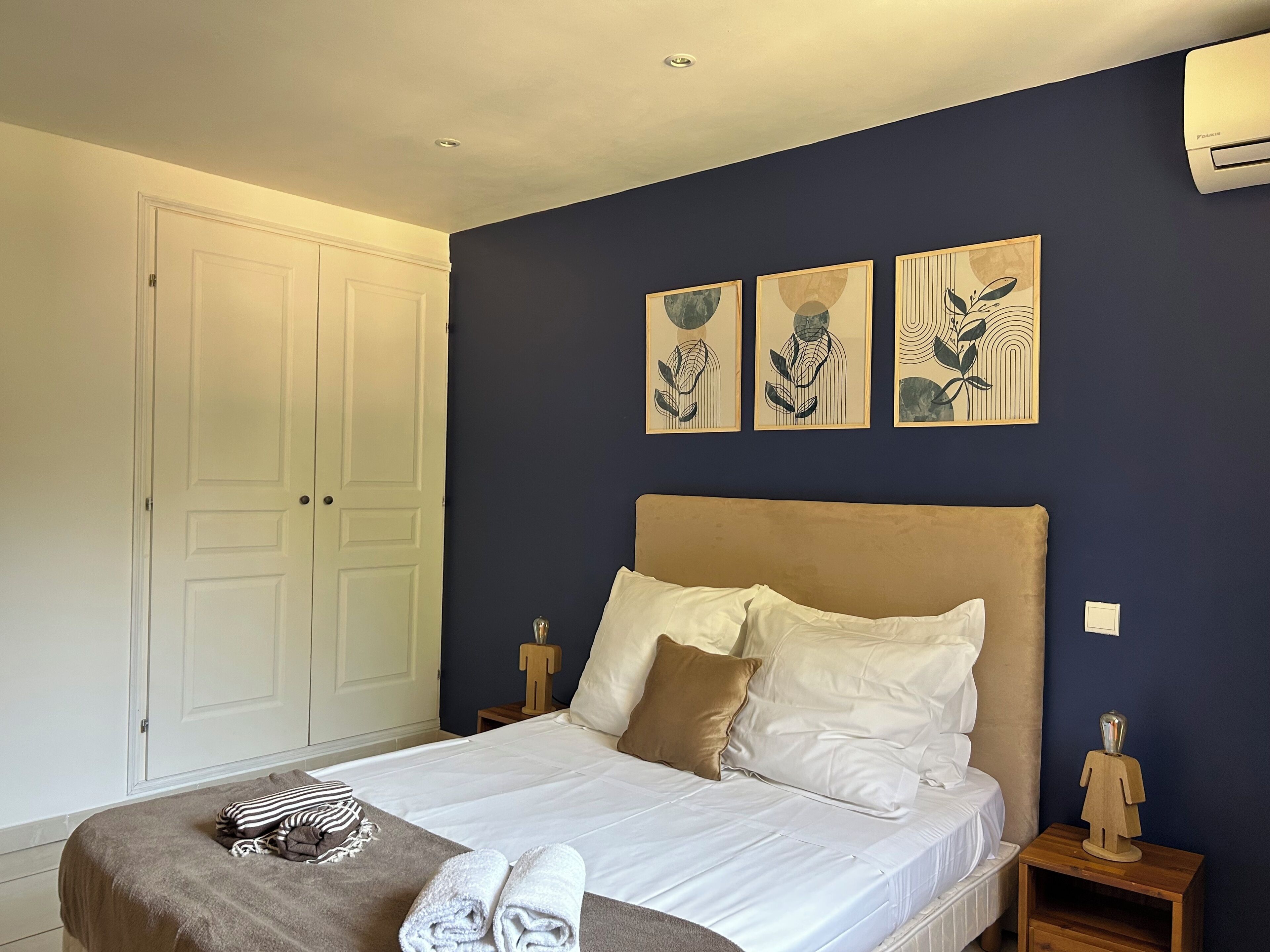 A bedroom with a bed, a wardrobe, and three wall-mounted artworks.
