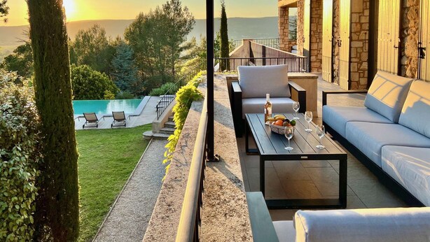 Eine Terrasse mit Gartenmöbeln, einem Pool und einem Steinhaus mit Fensterläden.