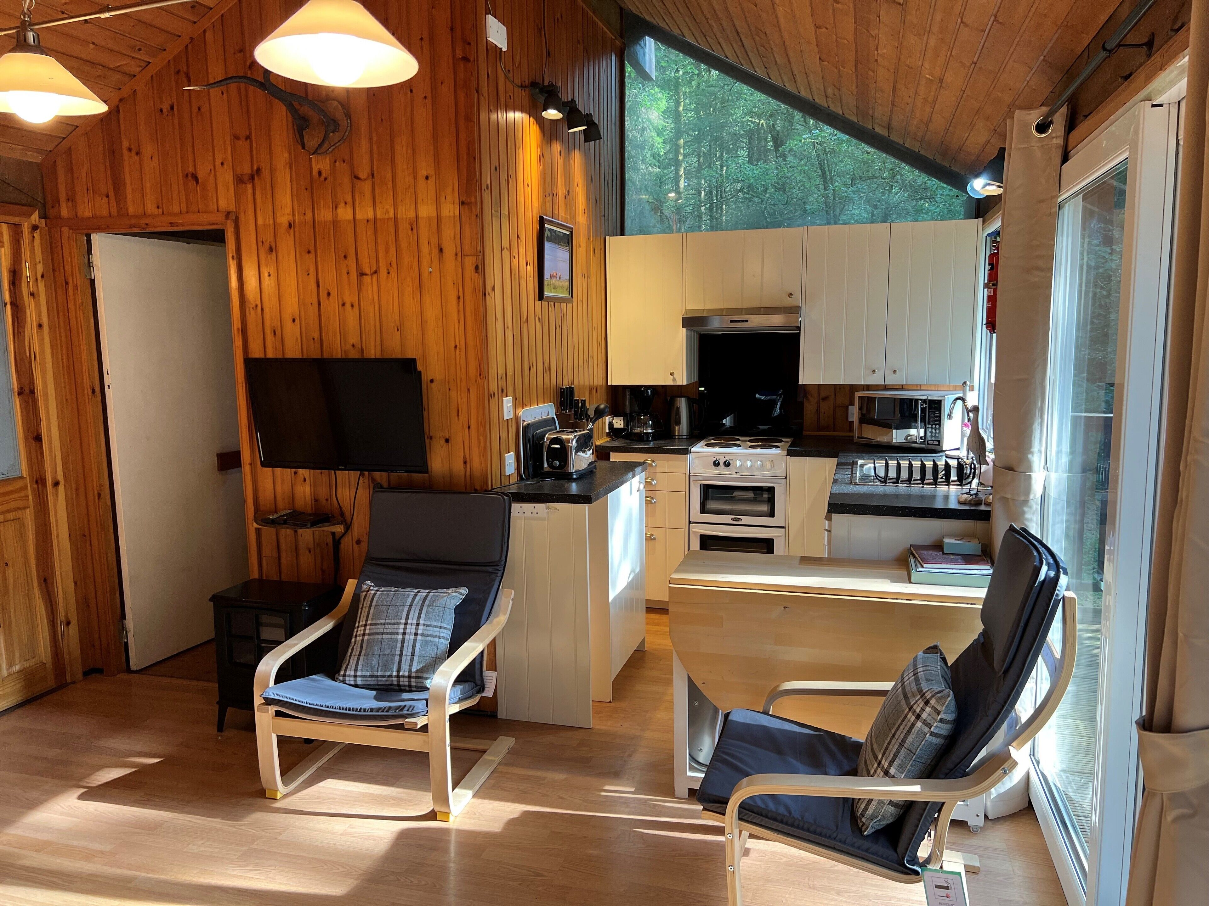 Un intérieur chaleureux de style cabane, avec des murs en bois, un coin cuisine et deux fauteuils inclinables.
