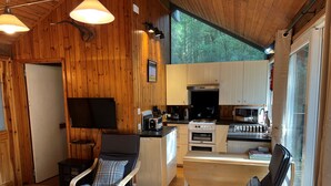 A cozy cabin-style interior with wooden walls, a kitchen area, and two reclining chairs. - KINGLAS CABIN is in a lovely, peaceful location deep in the forest, with hot tub (Dalavich)