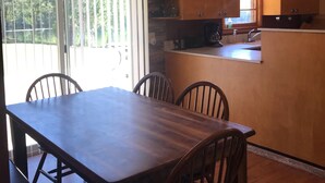 Un comedor con una mesa y sillas de madera, un ventilador de techo y una cocina con armarios de madera y un ventanal.