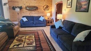 Una sala acogedora con un sofá azul, un tapete estampado y decoración de madera en la pared.