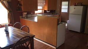Una cocina compacta con armarios de madera, un lavamanos integrado, un refrigerador y un comedor con mesa y sillas de madera.