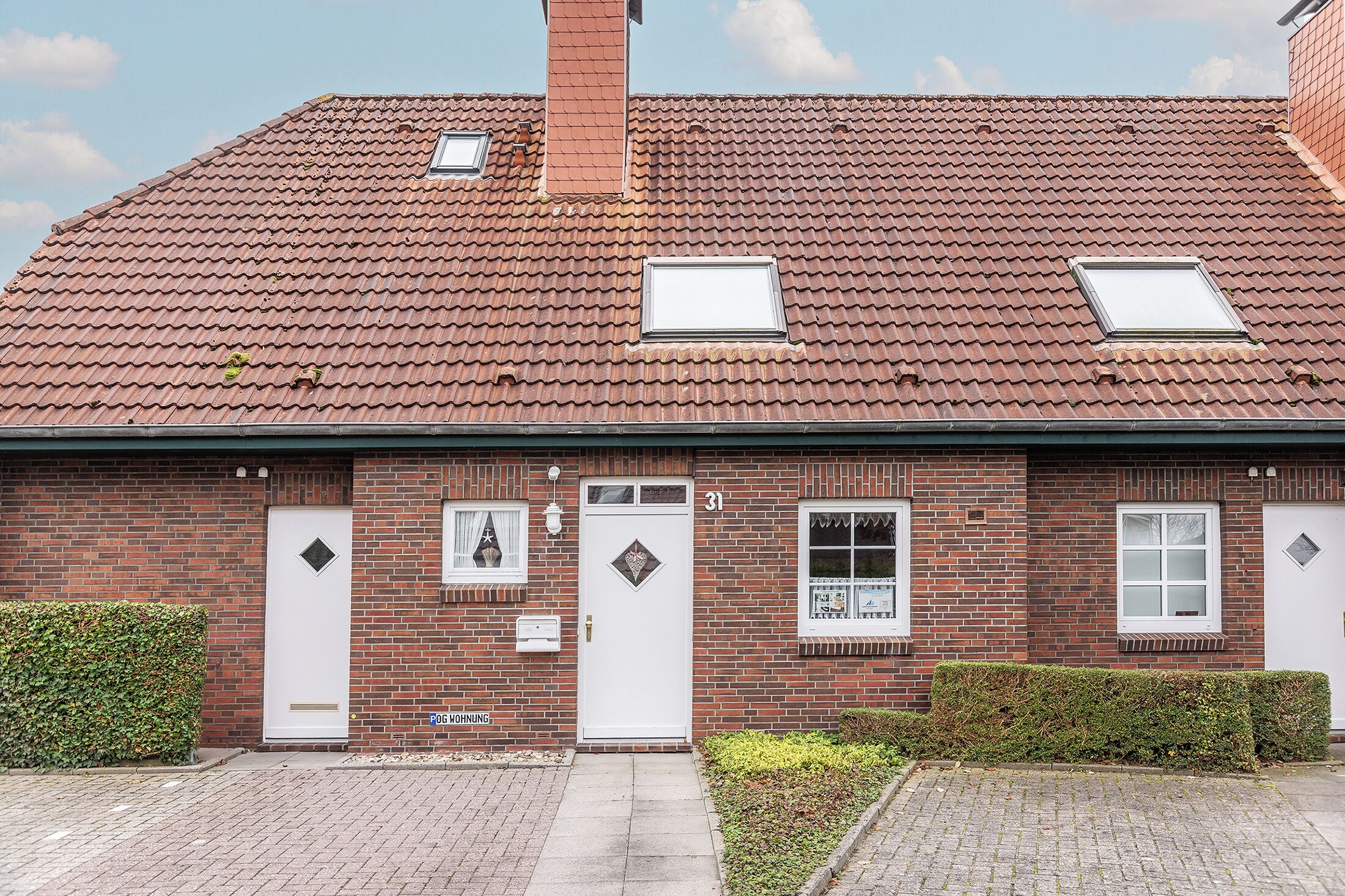 A two-story brick house with a red-tiled roof, two small dormer windows, and a white front door.