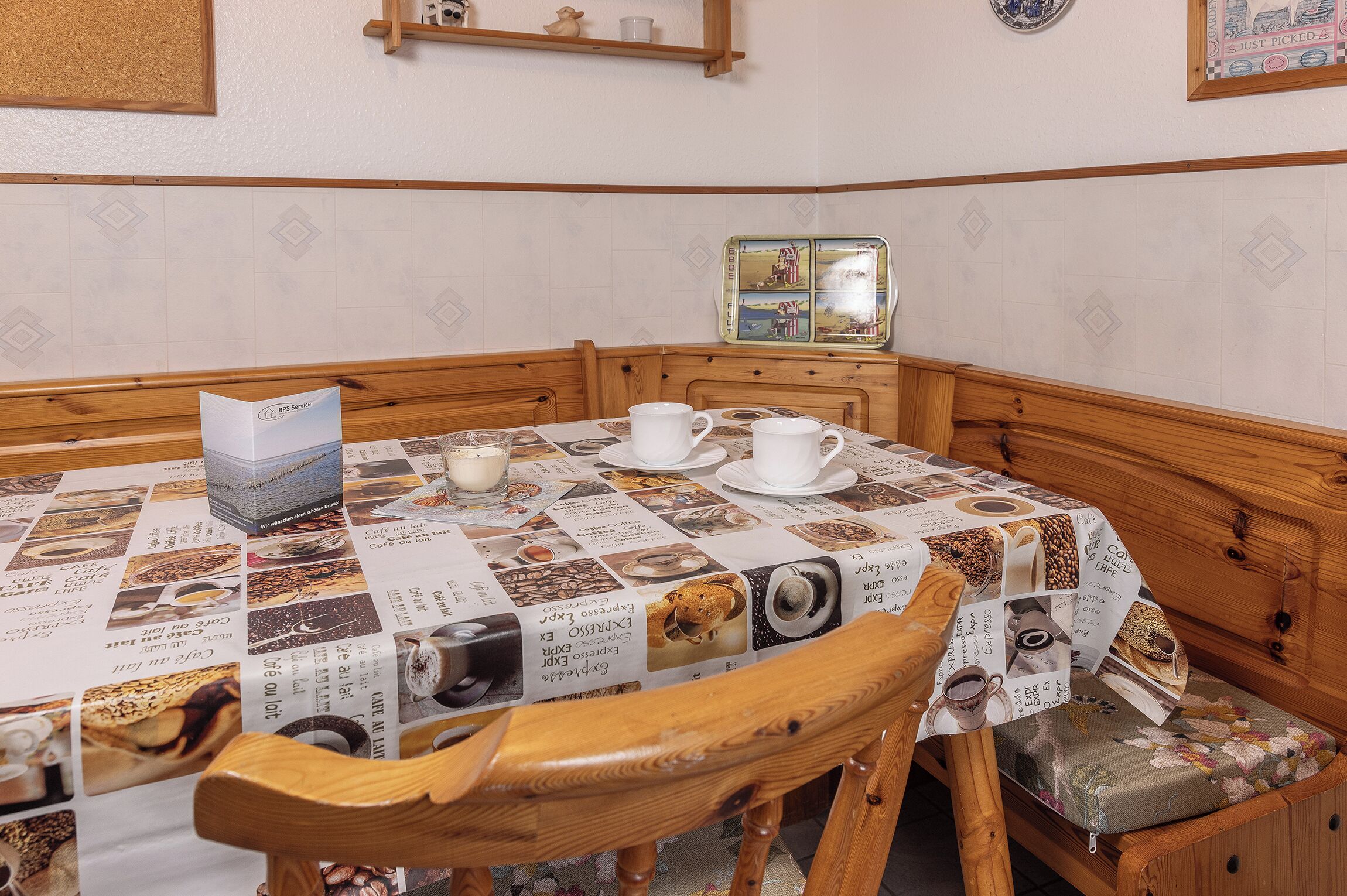 Un espace repas comprenant une table et des chaises en bois, un présentoir à menus et une étagère murale agrémentée d’objets décoratifs.