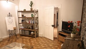 A living room with a herringbone floor pattern, a glass coffee table, a wooden sideboard, a television, and a bookshelf with various items. - Apartment Lindauer Löwe- Charming, close to the lake & central in a historic building (Lindau)