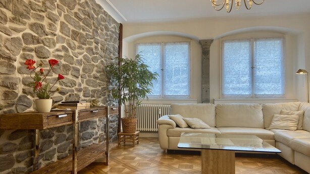 A living room with a stone wall, a sofa, a coffee table, and a chandelier. - Apartment Lindauer Löwe- Charming, close to the lake & central in a historic building (Lindau)