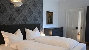 A neatly made bed with white linens in a room with patterned wallpaper, a dark headboard, and a painting on the wall. - Apartment Lindauer Löwe- Charming, close to the lake & central in a historic building (Lindau)