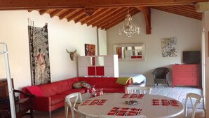 A dining area with a round table, white chairs, and a red sofa. There is a chandelier hanging from the ceiling and a television on a stand. - Studio beautiful view of the Pyrenees  (Souraïde)
