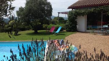 A swimming pool with lounge chairs, a covered patio, and a view of the surrounding landscape.