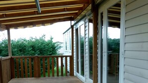 A covered deck with wooden railings and a view of a house through glass doors.