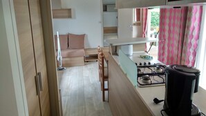 A compact kitchen with a gas stove, a coffee maker, and a sink. There is a wooden bench and a sofa in the adjacent living area.