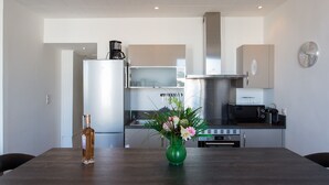A modern kitchen with stainless steel appliances, a dining table with a vase of flowers, and a clock on the wall. - CANNES CENTER, IDEAL CONGRESS, HOLIDAYS, MODERN APARTMENT FACING THE OLD PORT (Cannes)