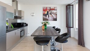 A modern kitchen with a dining area, including a table with chairs, a clock, and a painting on the wall. - CANNES CENTER, IDEAL CONGRESS, HOLIDAYS, MODERN APARTMENT FACING THE OLD PORT (Cannes)