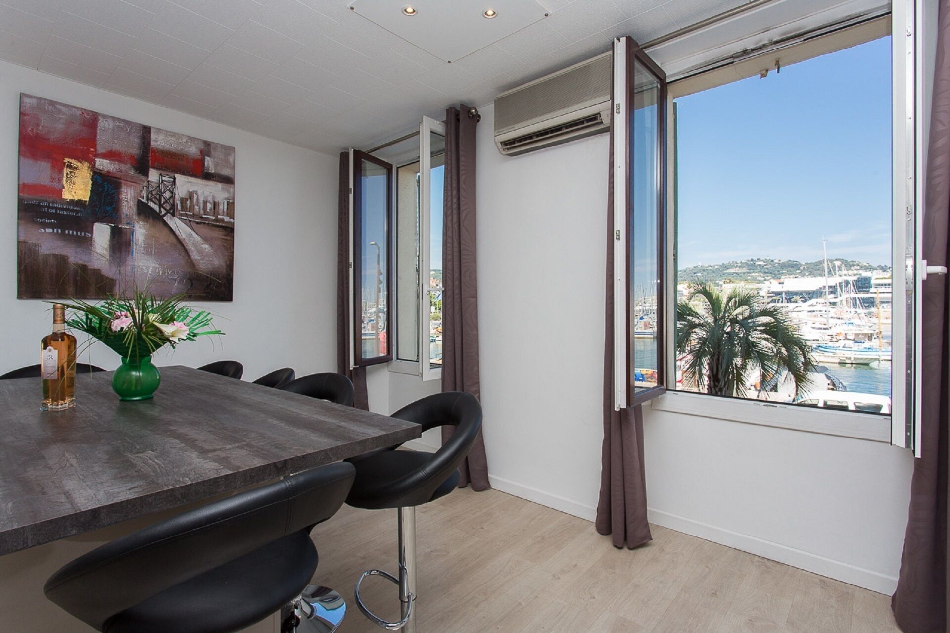 A modern room with a dining table, chairs, a vase with flowers, and large windows with curtains.